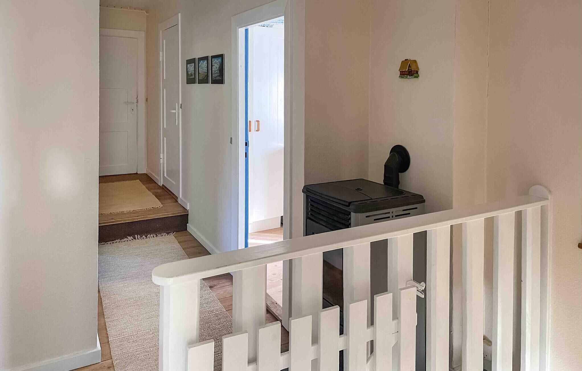 A hallway with a white railing, a door at the end, and a small black object on a white surface.