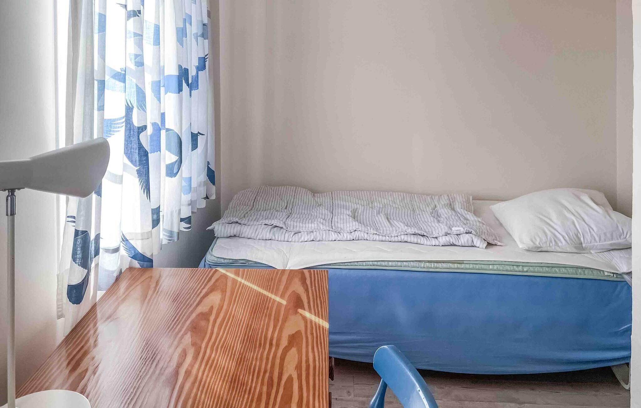 Une petite pièce simple, avec un lit, une table et une chaise.