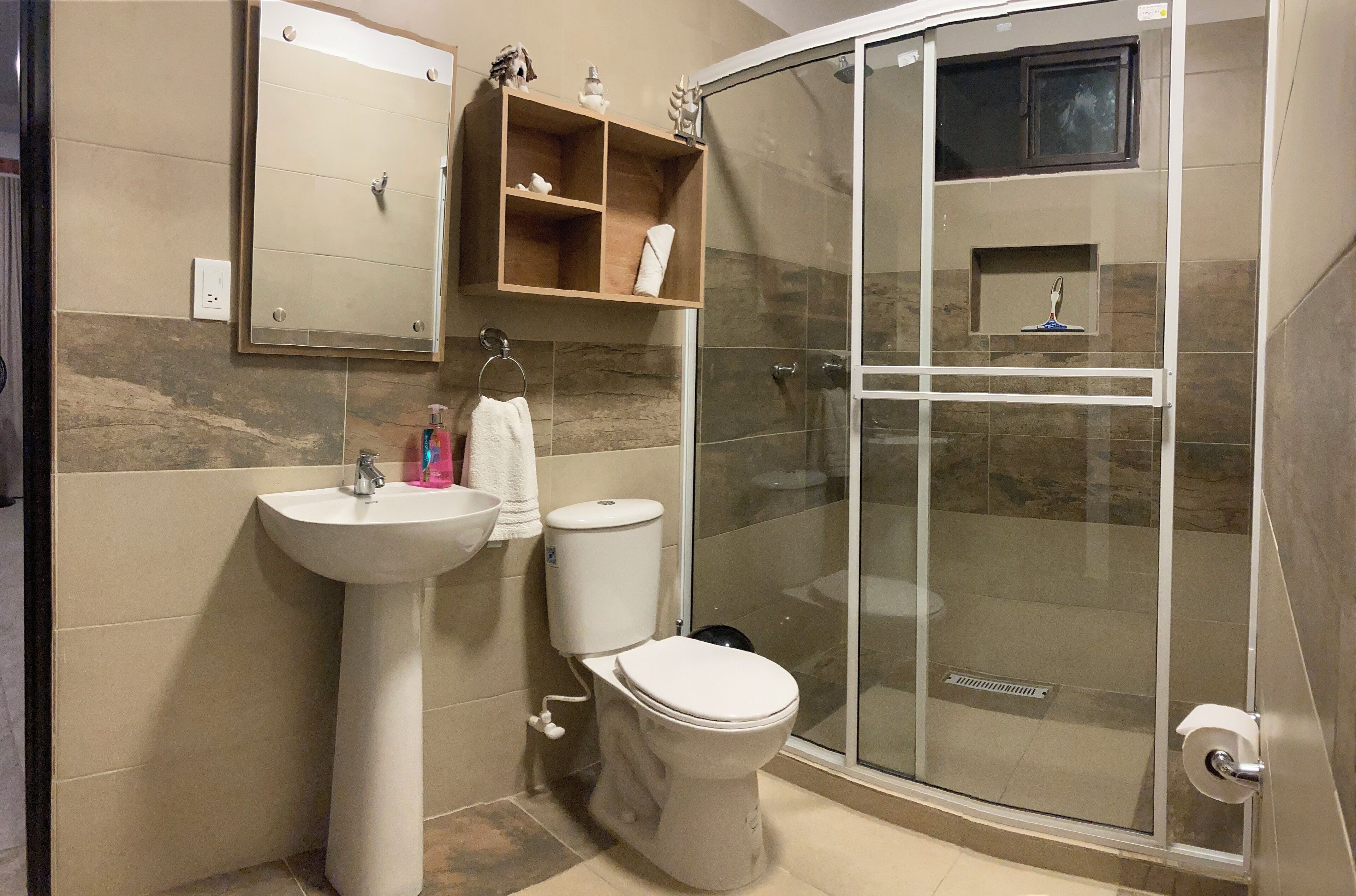 Un baño con ducha de vidrio, lavamanos pedestal y retrete.
