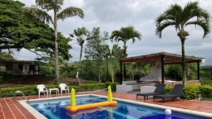 Una piscina con azulejos azules, rodeada por un suelo de ladrillo y una zona cubierta con sillas de descanso.