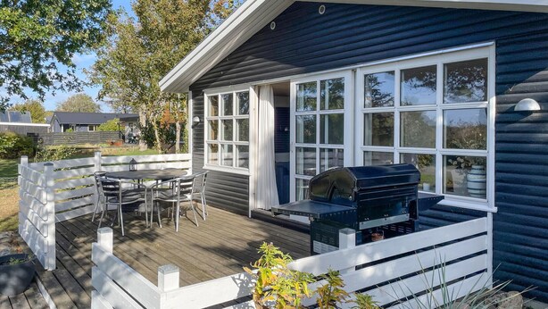 A deck with a grill and a table, surrounded by a white fence.