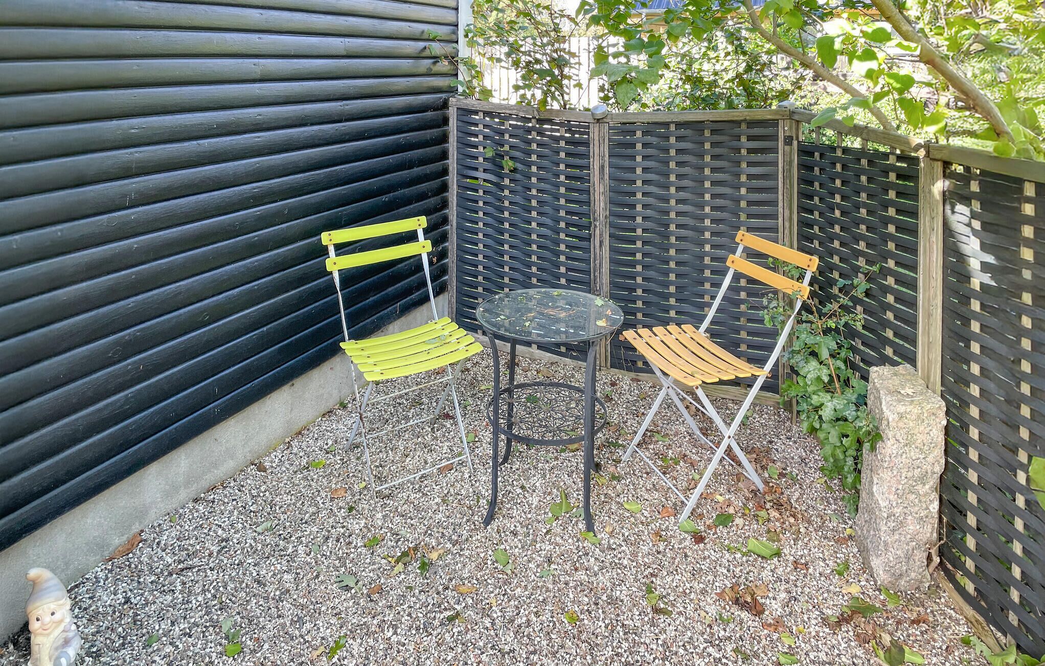 A small outdoor seating area with a metal table and two chairs, surrounded by a black fence and gravel ground.
