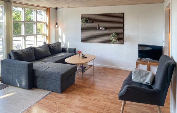 A modern living room with a sectional sofa, a round coffee table, a TV, and a wall-mounted shelf with plants. - Beautiful home in Millinge with WiFi (Millinge)