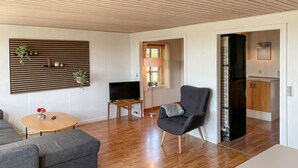 A modern living room with a flat-screen TV, a grey armchair, a wooden coffee table, and a sofa.