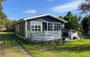 A small, single-story cabin with a sloped roof, a front porch with white railings, and a stone foundation. - Beautiful home in Millinge with WiFi (Millinge)