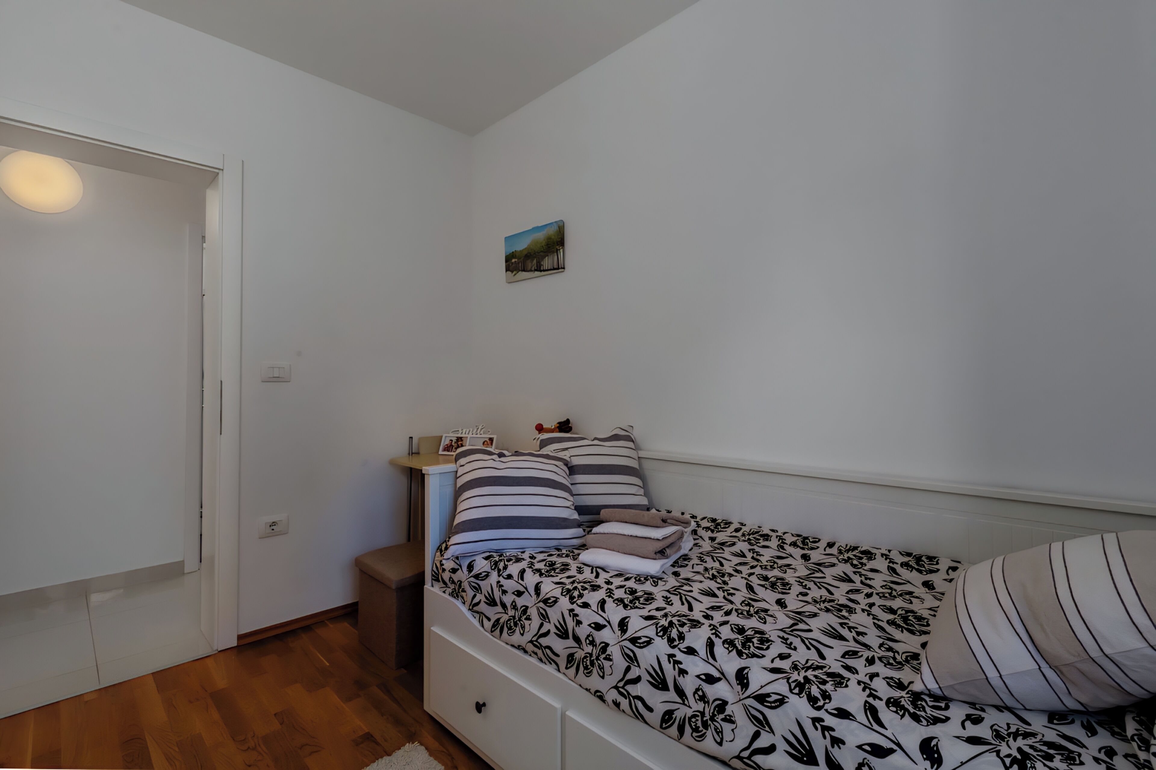 Une chambre à coucher avec un lit simple, une table de chevet, une petite table d’appoint et un tableau accroché au mur.