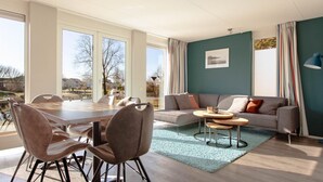 A modern living room with a dining area, large windows, a teal accent wall, and a view of the outdoors.