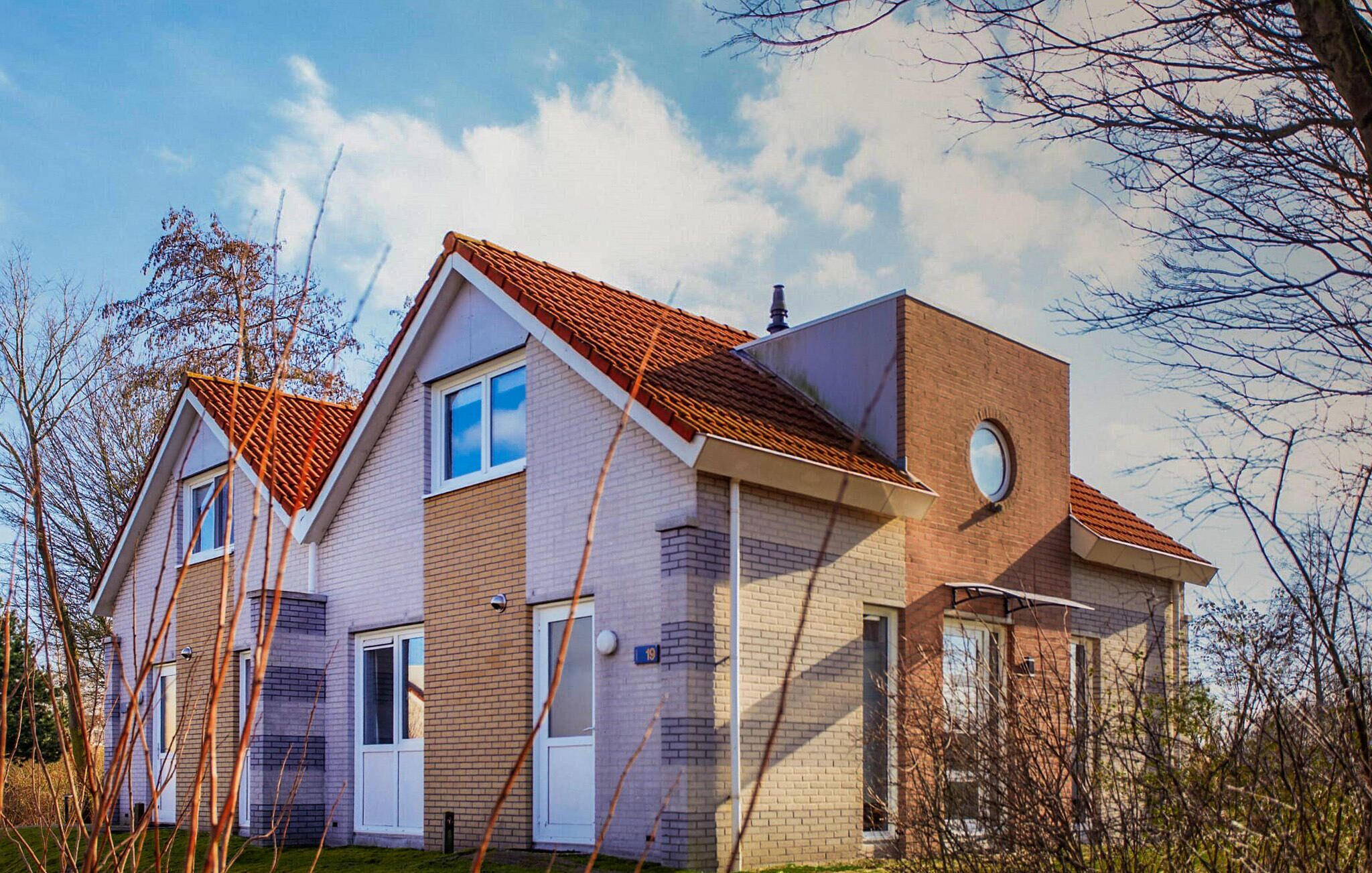 Een twee verdiepingen tellend huis met een rode dakbedekking van tegels, een gevel van baksteen en een rond raam op de tweede verdieping.