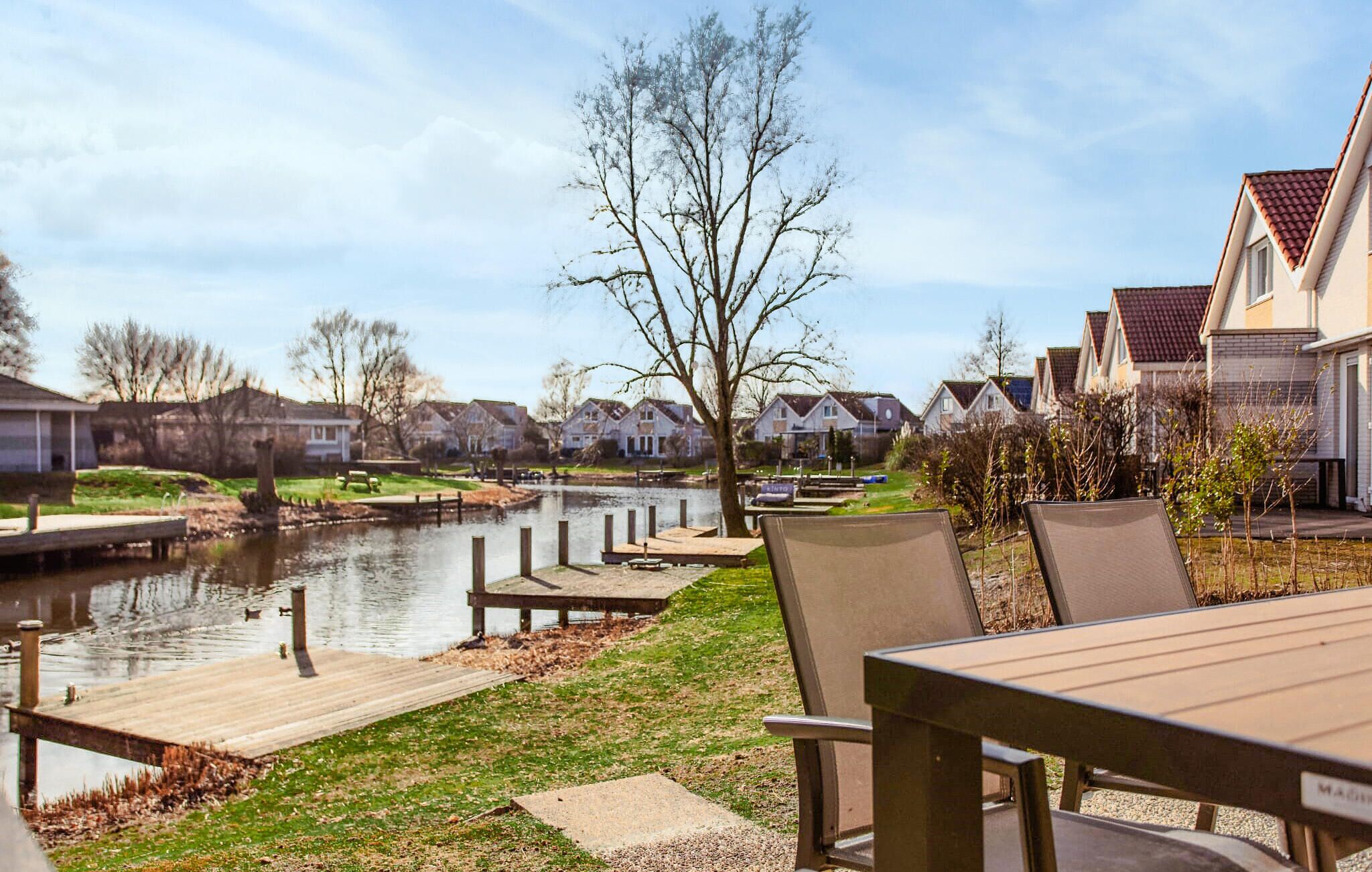 A riverside park with a wooden dock, chairs, and a grassy area.