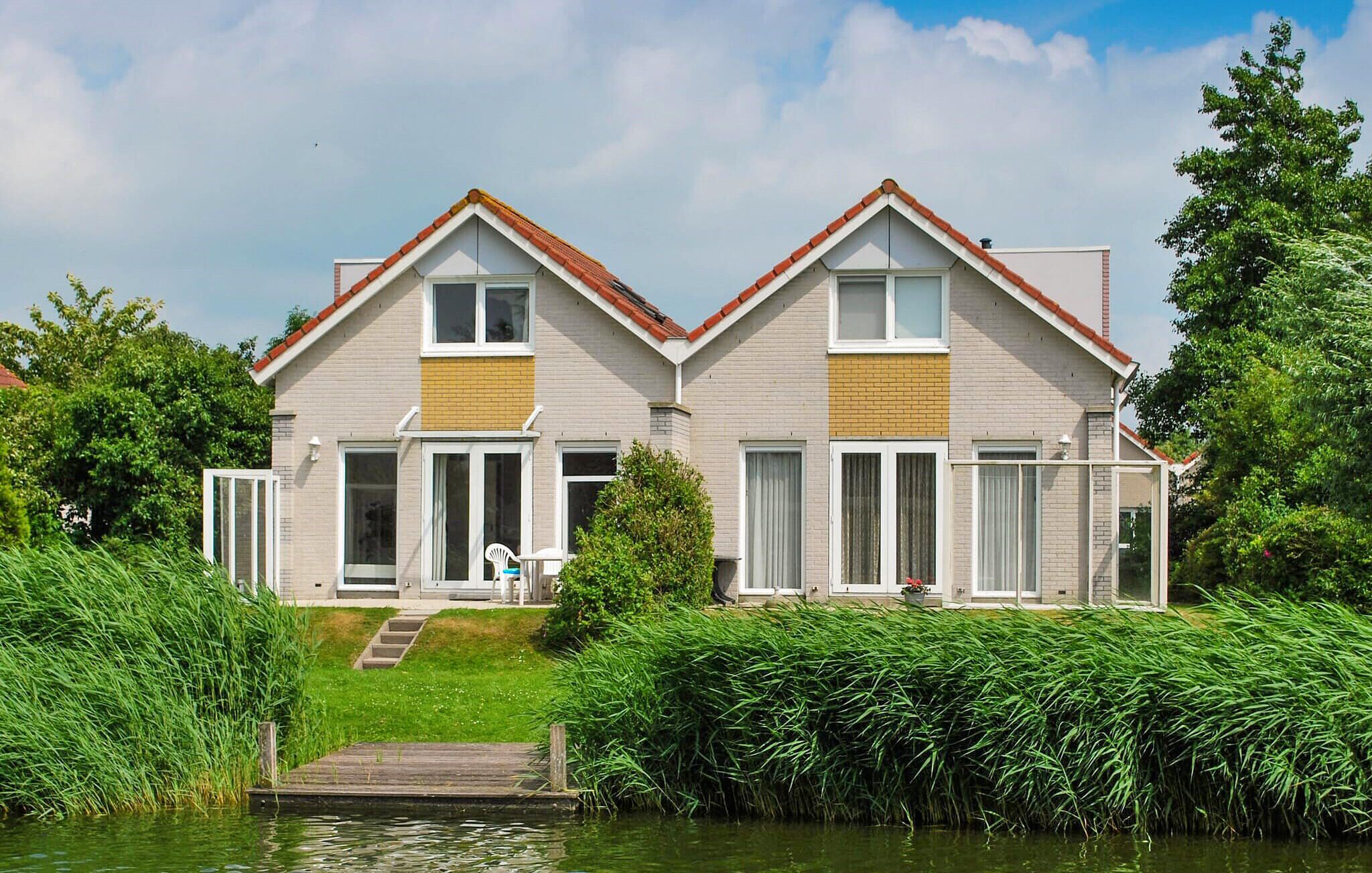 A two-story house with a gabled roof, large windows, and a wooden dock leading to a water body.