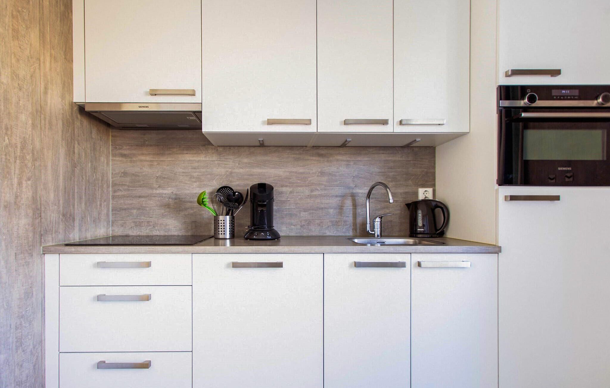 Una cocina moderna con gabinetes blancos, un lavamanos de acero inoxidable y una cafetera Siemens.
