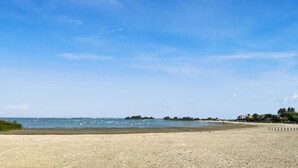 A beach with a clear sky, calm water, and distant buildings.