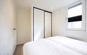 Un dormitorio con cama, puerta corredera, ventana con persianas y radiador.