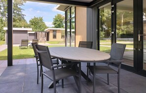 Un patio al aire libre con una mesa redonda y cuatro sillas, rodeado por puertas y ventanas de vidrio.