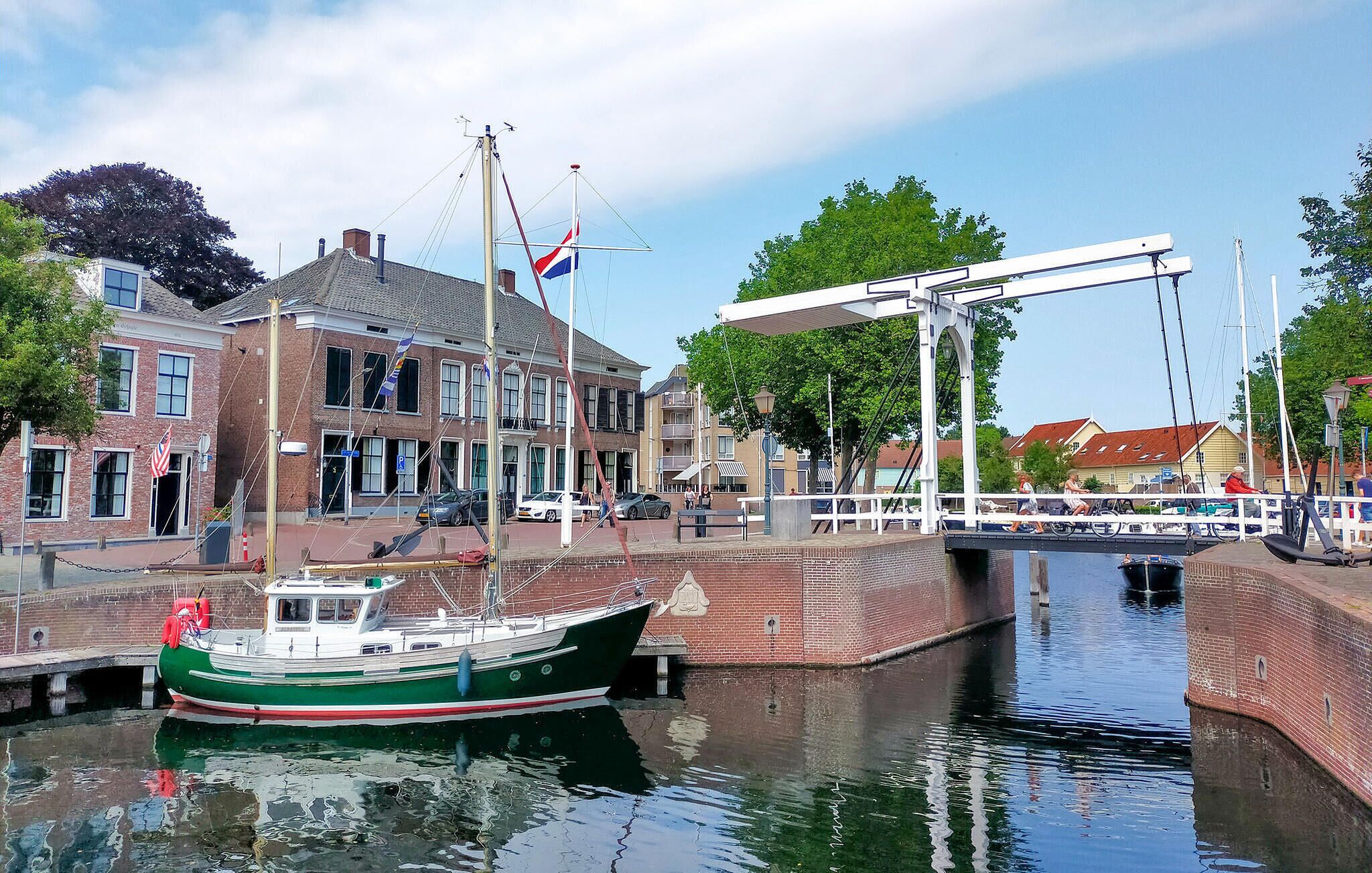 Un canal où est amarré un bateau vert, un pont et des bâtiments ornés de drapeaux.