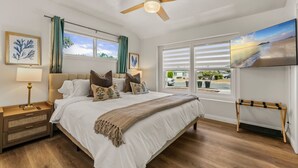Een slaapkamer met een bed, een plafondventilator, een televisie en een raam met uitzicht.