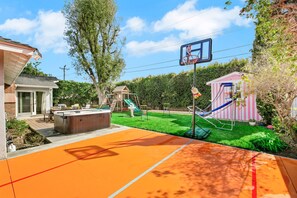 A backyard with a basketball court, hot tub, slide, and play structures.