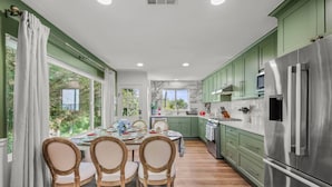 Una cocina con gabinetes verdes, un refrigerador de acero inoxidable y una mesa de comedor preparada para cuatro personas.