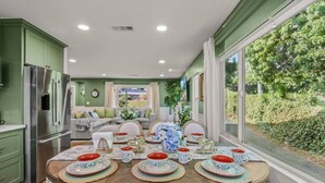 Comedor con mesa de madera dispuesta para cuatro personas, rodeado de armarios verdes y un amplio ventanal con vistas a la vegetación.