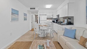 Eine moderne, weiß eingerichtete Wohnung mit Essbereich, Küche und Wohnzimmer.