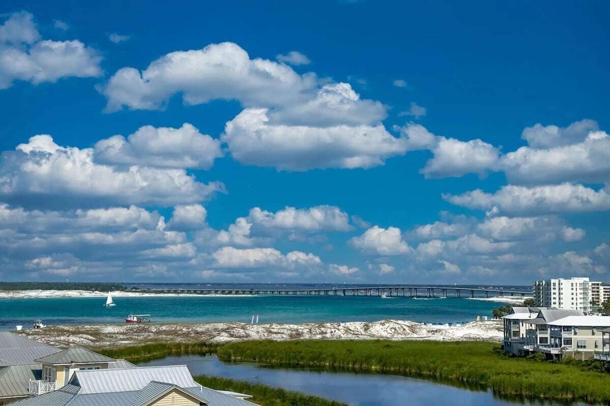 A coastal view with a bridge, a lighthouse, and buildings near the water.
