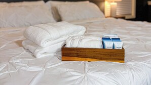 Un lit bien fait, avec du linge de lit blanc et un plateau en bois contenant des articles de toilette.