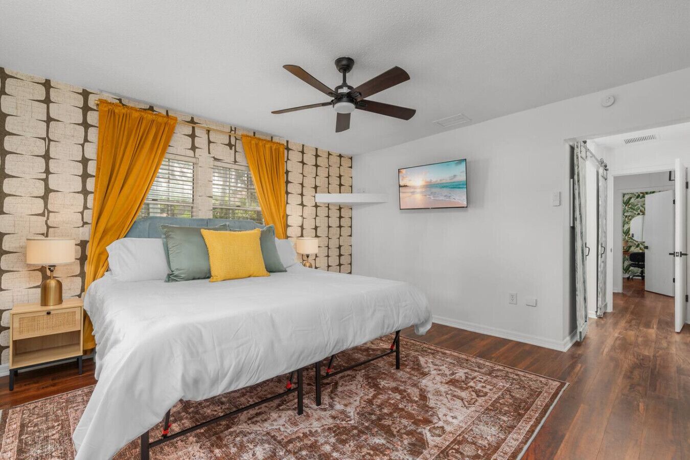 Ein Schlafzimmer mit Bett, Deckenventilator, Nachttisch, Lampe, Teppich und einem Bild an der Wand.