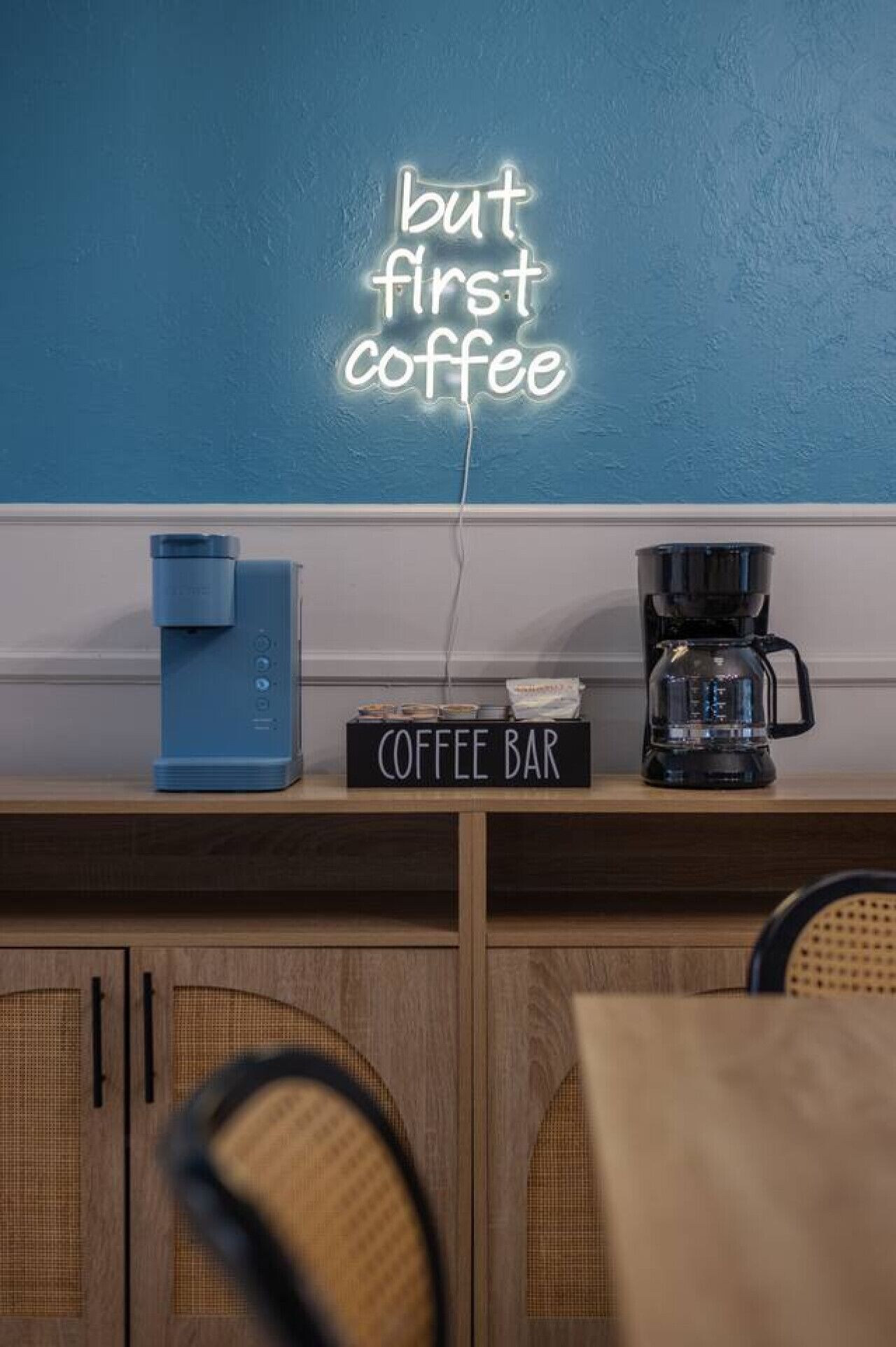 A coffee bar with a neon sign reading "but first coffee" and a coffee machine.