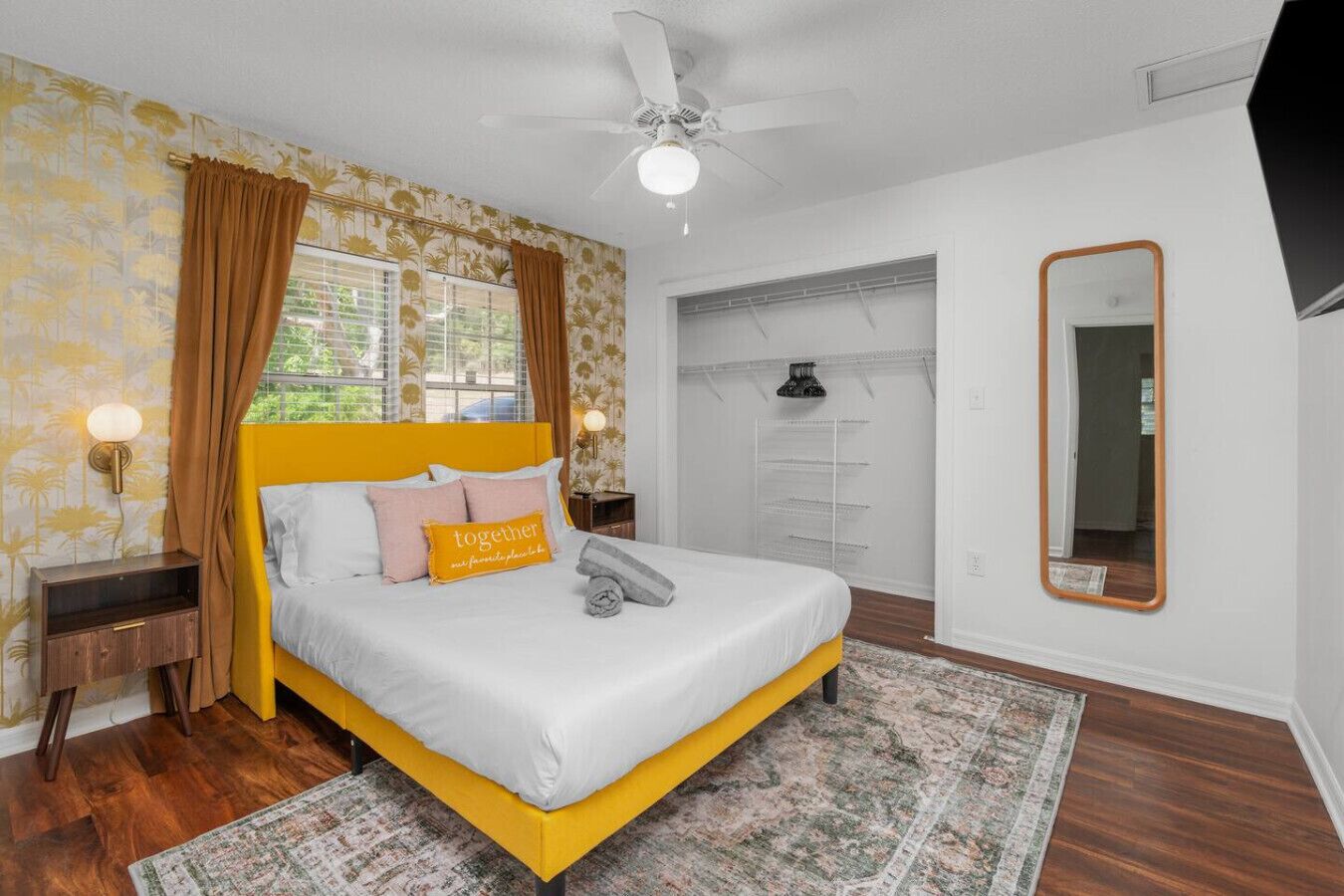 A bedroom with a bed, a ceiling fan, a wardrobe, and a mirror.