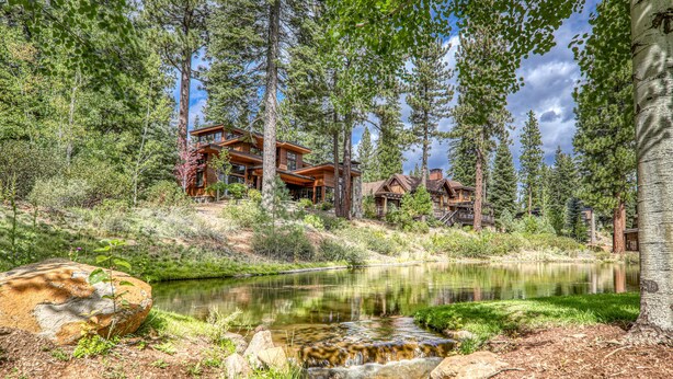 A lodge with a wooden exterior, surrounded by tall trees and a small stream. - Monthly Lease - Ambiance at Martis Camp by Tahoe Getaways - 4BR w/ Hot Tub & Bonus Room (Truckee)