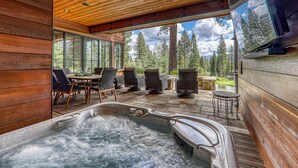 A wooden interior with a hot tub, outdoor seating, and a view of trees. - Monthly Lease - Ambiance at Martis Camp by Tahoe Getaways - 4BR w/ Hot Tub & Bonus Room (Truckee)