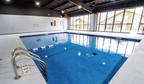 An indoor swimming pool with clear water, a metal ladder, and large windows.