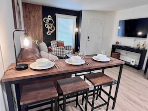 Un coin repas avec une table en bois dressée pour quatre personnes, un canapé et un téléviseur en arrière-plan.