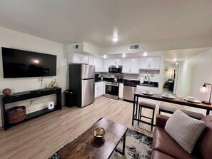 A modern kitchen with white cabinets, stainless steel appliances, and a dining area with a wooden table and a leather couch.