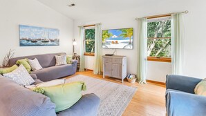 Una sala de estar con sofá, sillones, televisor y ventana con vista a árboles.