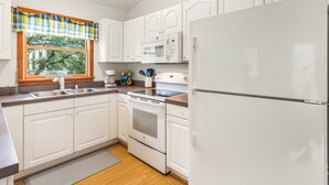 Una cocina moderna con armarios blancos, un lavamanos de acero inoxidable, un microondas, una estufa y un refrigerador.