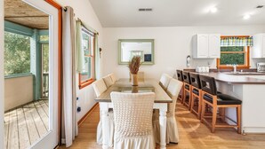 Una cocina moderna con comedor, que incluye una mesa de vidrio, sillas blancas con tapicería y piso de madera.