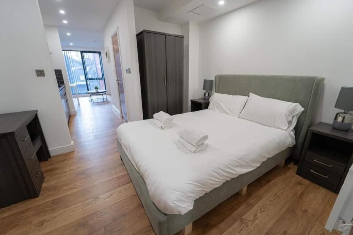 A modern bedroom with a large bed, bedside tables, a wardrobe, and a view to a balcony.