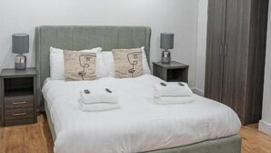 Ein modernes Schlafzimmer mit einem grau gepolsterten Bett, zwei Nachttischen mit Lampen, einem Kleiderschrank und einem Holzboden.