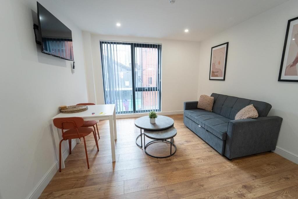 A modern living room with a grey sofa, a round coffee table, and a dining area with a white table and red chairs.