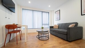 Ein modernes Wohnzimmer mit grauem Sofa, einem kleinen runden Tisch und einem Essbereich mit weißem Tisch und orangenen Stühlen.