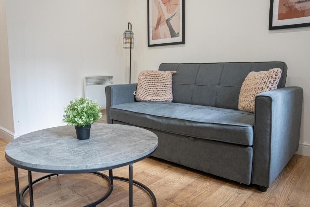 Ein graues Sofa mit zwei Kissen, ein kleiner runder Tisch mit einem Topf und ein an der Wand befestigter Heizkörper.