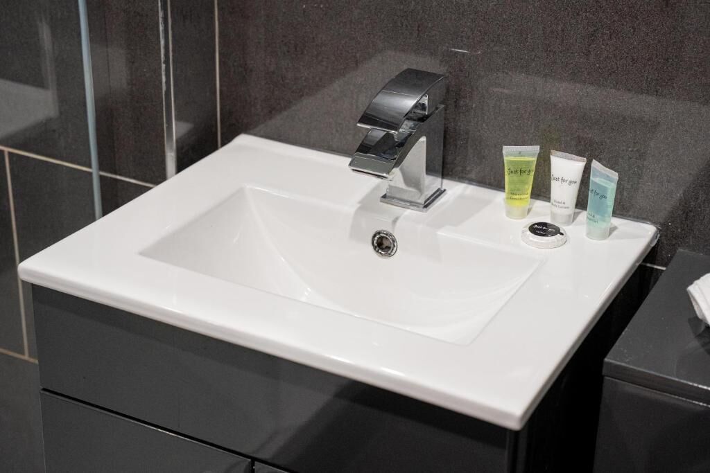 Ein weißes Waschbecken mit einem modernen Wasserhahn und drei Pflegeprodukten auf der Ablagefläche.
