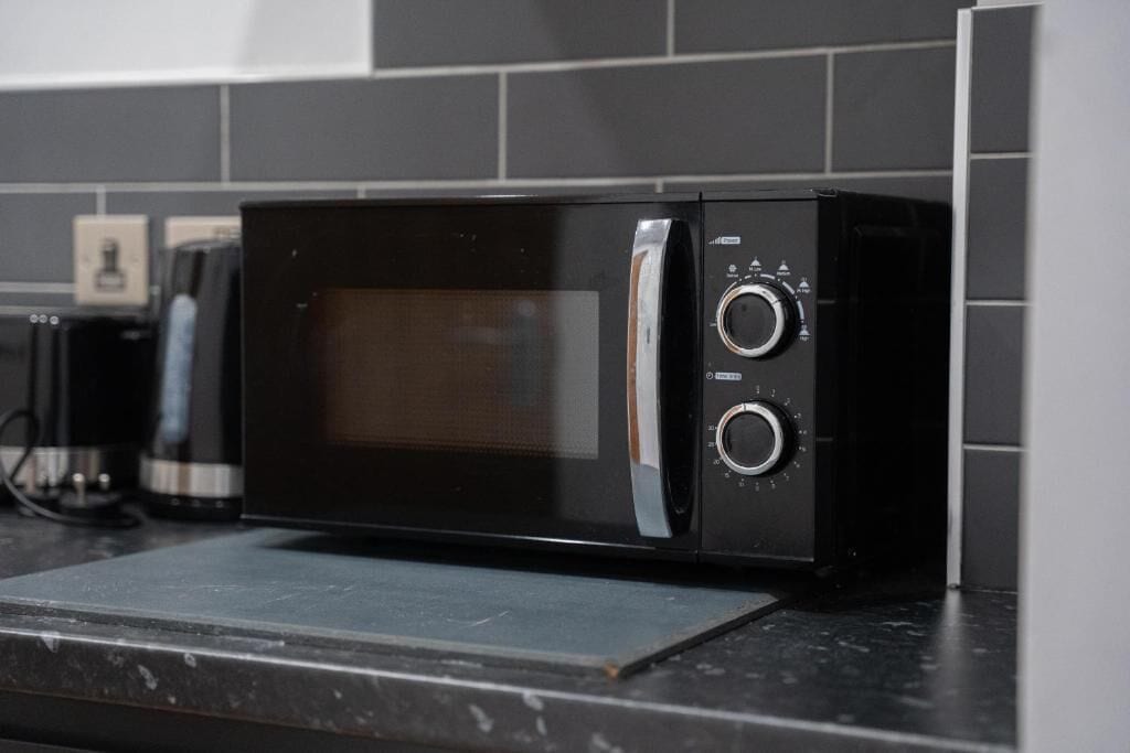 Un horno microondas negro sobre una encimera de cocina con salpicadero de azulejos.