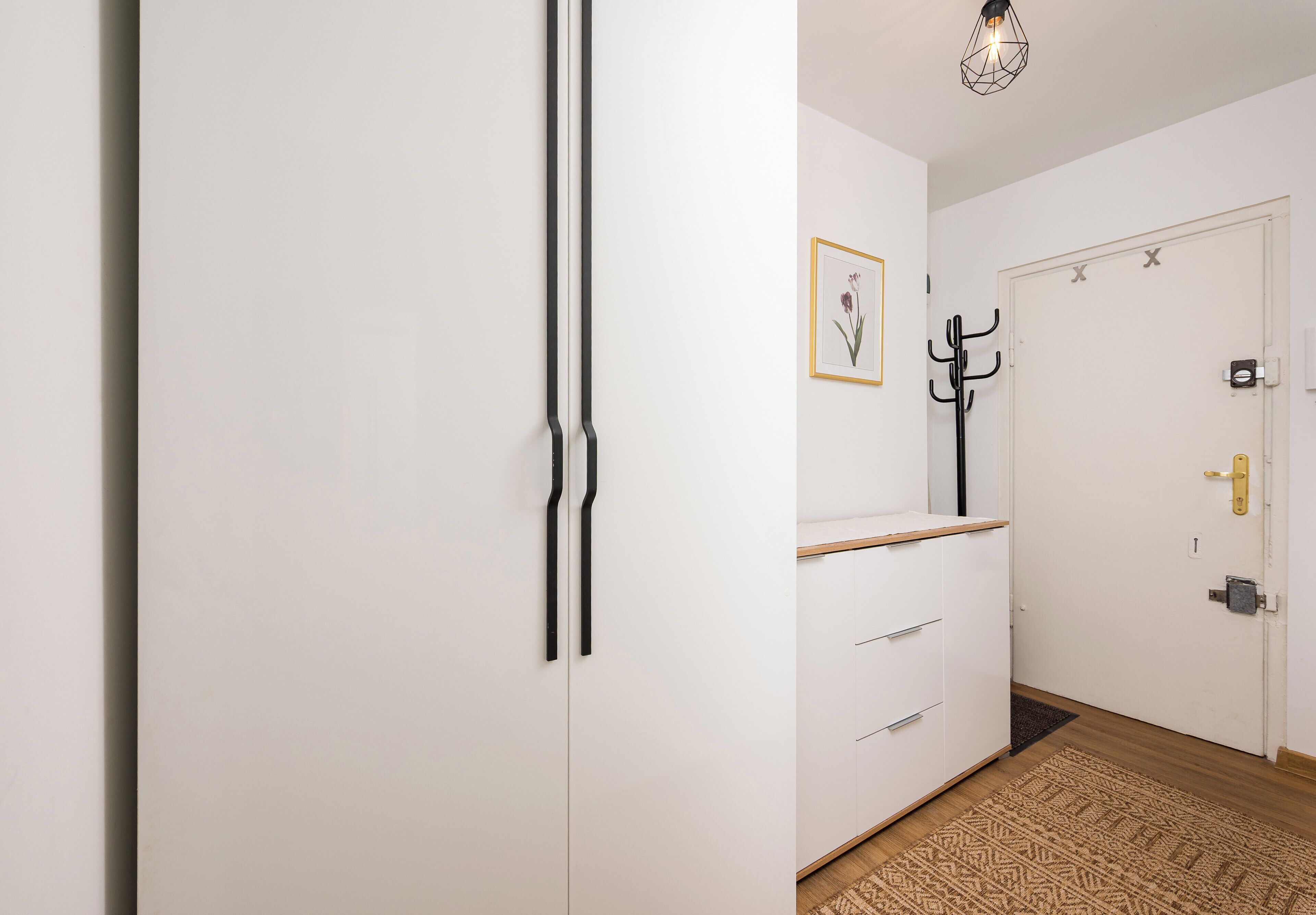 A hallway with a white wardrobe, a coat rack, and a door with a coat hanging.