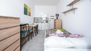 Una camera compatta con un letto, una scrivania, una sedia, un angolo cottura e uno scaffale.