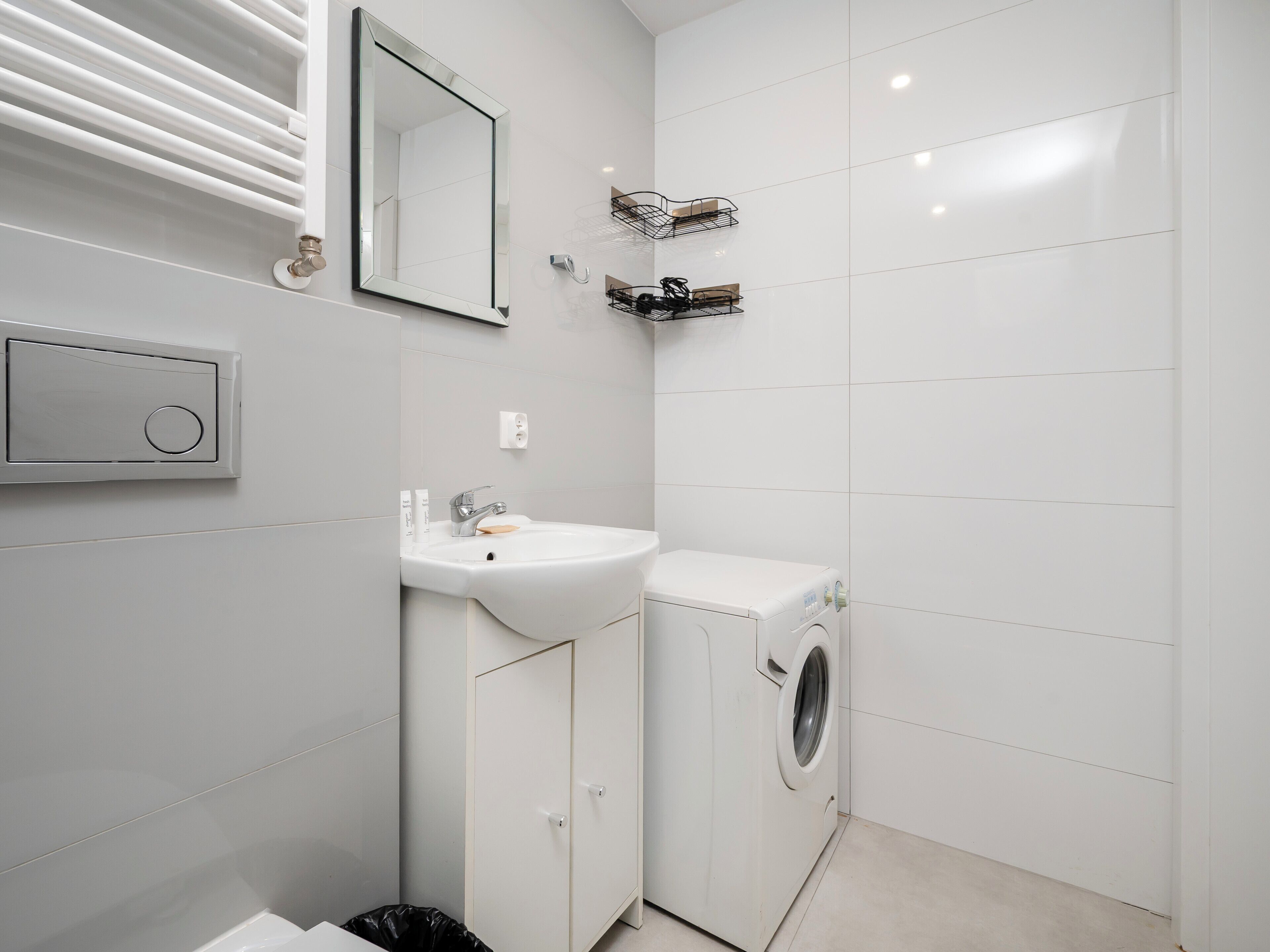 A modern bathroom with a white sink, mirror, and washing machine.