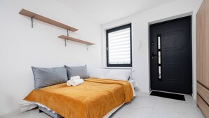 Un dormitorio con cama, almohadas, una colcha, una ventana, una puerta y una estantería.