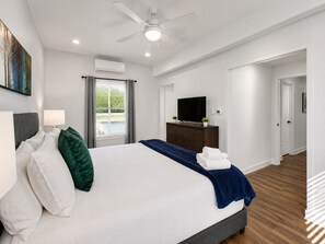 A modern hotel room with a large bed, a flat-screen TV, a ceiling fan, and a window with blinds.