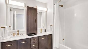 Un baño moderno con un espejo grande, un tocador de madera oscura, un lavabo blanco y una zona de ducha.